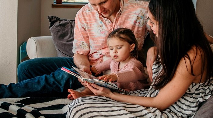 bố và mẹ đọc sách cho bé gái trên ghế sofa, học ngoại ngữ