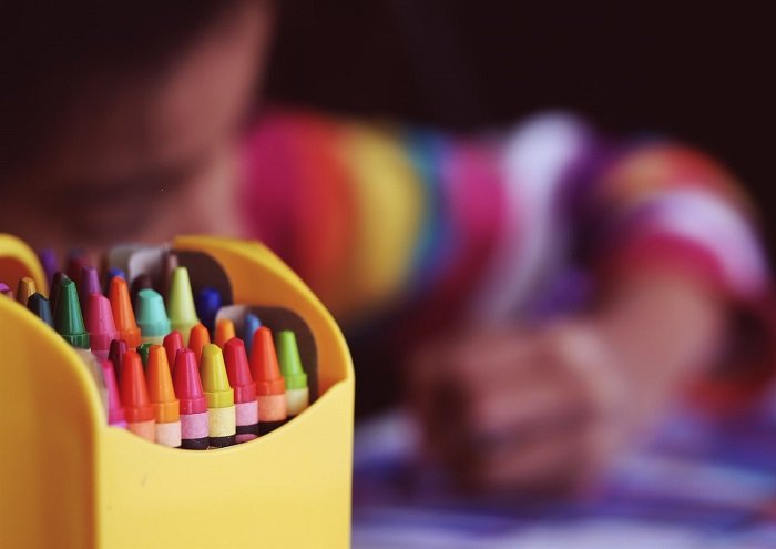 Em bé ngồi học bên hộp bút màu.